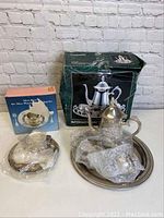 Photo of silver plated tea set with teapot and tray in original green box, showing tarnish and wear, with items partially wrapped in plastic.