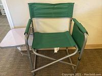 Front view of the green folding chair showing the fold-out side tray on the right armrest and fabric seat and backrest.