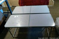 Two white folding tables side by side, showing tops and legs folded out