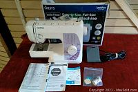 Brother LX2375 sewing machine with box, manual, foot pedal, power cord, and small accessories displayed on a wooden floor.