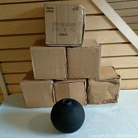 Stack of five cardboard boxes with one black round vase displayed in front. Boxes are marked as containing black vases.