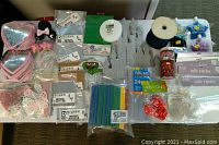 Various arts and crafts supplies arranged on table including sequined hearts, foam snowmen, beads, ribbons, pipe cleaners, straws, tulle circles, butterflies, and rose buds.