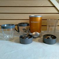 Nutribullet Magic Bullet blender base, two clear plastic cups, one with handle, and two stainless steel blade attachments shown from front