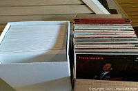 Two boxes containing approximately 100 assorted LP vinyl record albums. One box filled with albums in original and generic sleeves, the other box is mostly empty or filled with white sleeves.