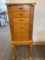 Front view of the tall wooden jewelry armoire with five drawers and two side doors, standing on curved legs.
