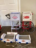 Cotton candy stand next to Coca-Cola cooler cart and two hot dog rollers on floor.
