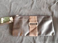 Front view of the brown Roots clutch showing textured leather material with suede accent, silver-tone buckle detail, and wrist strap attached to zipper.