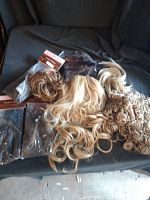 Lot of fancy hair weaves with attached comb clips in various shades and styles displayed on dark fabric.