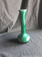 Side view of the tall green Blue Mountain Pottery vase showing the elongated neck and rounded base on a black fabric background.
