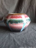 Photo of round colorful glazed pottery vase with a drip pattern in pink, green, and black hues.