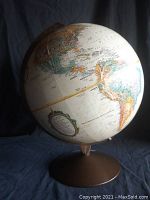 Off-white vintage world globe showing North and South America positioned on a brown metal stand.