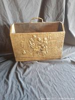 Photo of brass newspaper box front with embossed detailed European family scene and wood handle.