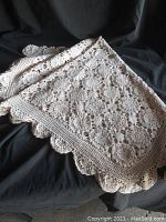 Full view of folded hand crocheted square tablecloth showing overall color and texture, laid on dark fabric background to highlight details.