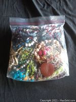 Bag filled with various bead jewelry including wood-toned, blue, white, green, purple, and red beads visible through clear plastic bag.