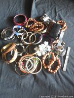 Variety of bracelets and bangles including wooden beads, metal bangles, fabric braided bracelets, and decorative pieces on a dark cloth background.