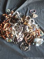 Photo of assorted jewelry with multiple necklaces, bracelets, rings, and brooches in a pile on dark fabric.