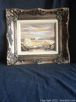 Front view of the framed oil painting showing ocean waves crashing on rocks with seagulls and an ornate gold frame.