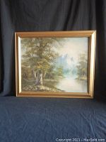 Framed oil on canvas landscape painting of a forest with a stream and rocky mountains in the distance.