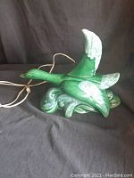 Full side view of vintage green ceramic goose lamp plugged in showing shape and finish.
