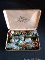 Vintage box open showing assorted costume jewelry pieces inside including brooches, earrings, and necklaces.