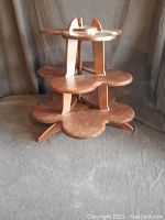 Three-level wooden display stand showing its overall shape and structure on a fabric backdrop.