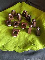 Top-down view of twelve teak wood napkin ring holders arranged on a green felt surface, showing their trapezoidal shapes and circular holes.