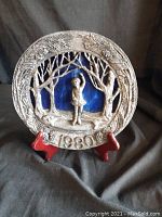 Full view of the 1980 pewter art plate with ice skating girl and stained glass background on red display stand.