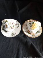 Two bone china teacup and saucer sets displayed on black fabric, showing front and side views