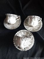 Three teacup and saucer sets arranged on black background showing silver floral pattern and shape.