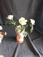 Overall view of the porcelain roses arranged in the decorative vase on a black fabric background.