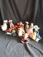 Wide view of 13 small porcelain dolls arranged in rows, showing a range of sizes 3 to 7 inches. Various dresses, bonnets, and hats.