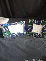 Two glass mosaic photo frames displayed on a black cloth background, showing rectangular and square shapes with blue and green glass tile mosaics in silver-toned metal frames.