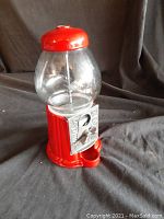 Full view of red metal candy or gumball machine with clear glass globe on top, sitting against a dark background