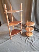 Photo showing the triangular three-level wooden display shelf next to the smaller round three-level shelf, both with natural wood finish and turned posts.
