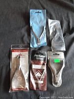 Four metal nail clippers sealed in plastic bags or blister packs, displayed on black surface.