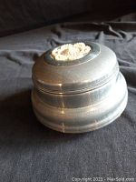 Top and side view of round vintage metal or pewter music jewelry box with a decorative bead rosette inset on the lid.