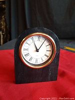 Arched black marble clock with round face showing Roman numerals and gold trim, on red fabric surface.