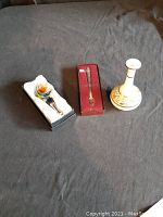 Photo showing the milk glass vase, colored glass bottle stopper in box, and Oneida small spoon in box arranged on a surface