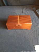 Closed rectangular mahogany wooden box with decorative inlay on top, placed on a dark fabric surface.