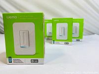 Four boxed Wemo Wi-Fi Smart Dimmer Light Switches arranged on white surface, front-facing boxes showing product image and brand.