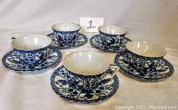 Five blue and white patterned teacups each paired with a saucer, arranged on a white surface.