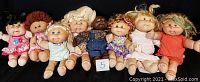 Eight assorted Cabbage Patch dolls arranged seated in a row showing all dolls included in the lot