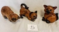 Photo of three wood cat figurines showing different poses and polished brown finish with black accents.