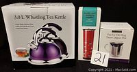 Photo showing boxed 3.0 L whistling tea kettle with purple metallic finish, boxed red double wall insulated stainless steel travel tumbler with heart pattern, and boxed clear glass tea mug with basket steeper.