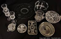 Photo of assorted crystal and glass items arranged on black background showing bowl, platter, pitcher, stemmed glasses, and various trays and dishes.