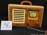 Front view of the antique Northern Electric radio showing the speaker grille, tuning dial with needle, two control knobs, and orange handle on top.