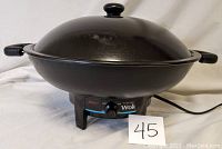 Photo showing the black electric wok with lid and temperature control knob on the base, plugged in and ready to use.