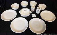 Overview of lot showing 4 white 10-inch plates, 4 white 6-inch bowls, 2 utensil holders labeled 'Paris', and 7-inch Corningware baking dish with clear Pyrex lid on black background.