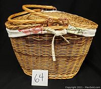 Wicker picnic basket with cloth lined interior and tied ribbon on the front. Basket has looped handles and a half-circle hinged lid.
