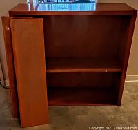 Solid wood bookcase with a detached shelf leaning against the case, showing the interior and shelf placements.
